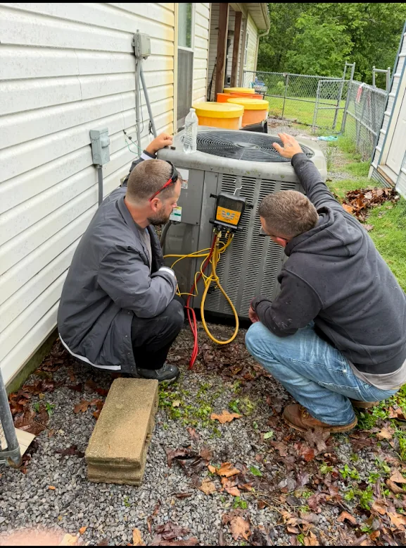 Two Stanphill Heating and Air technicians diagnosing a condenser unit with gauges outside a home